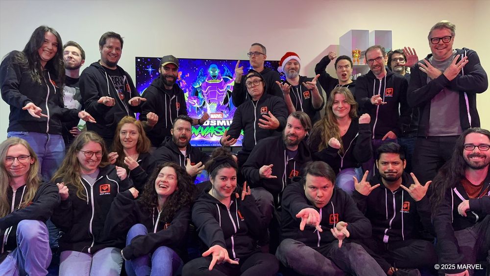Group photo of the Tribute Games team all wearing matching Tribute sweaters in front of the MARVEL Cosmic Invasion cover art