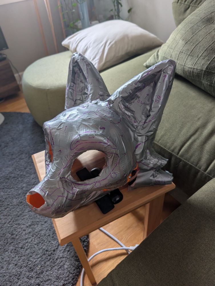 A 3D printed fursuit head base, covered in duct tape. Patterns are marked out in purple sharpie, with fur direction marked by arrows and fur colors noted