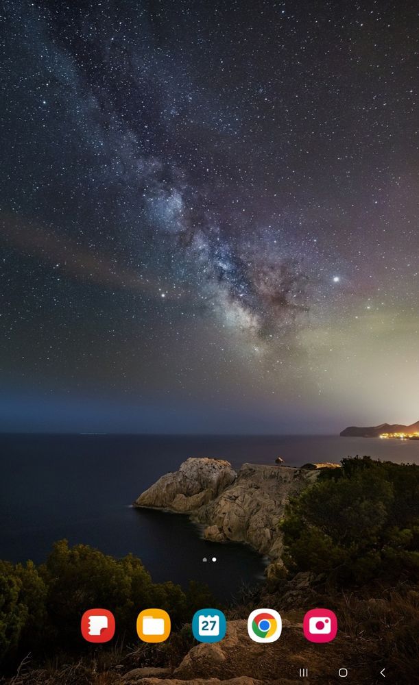 Looking over a cliff to the sea while the Milky Way and the stars shine in the sky.