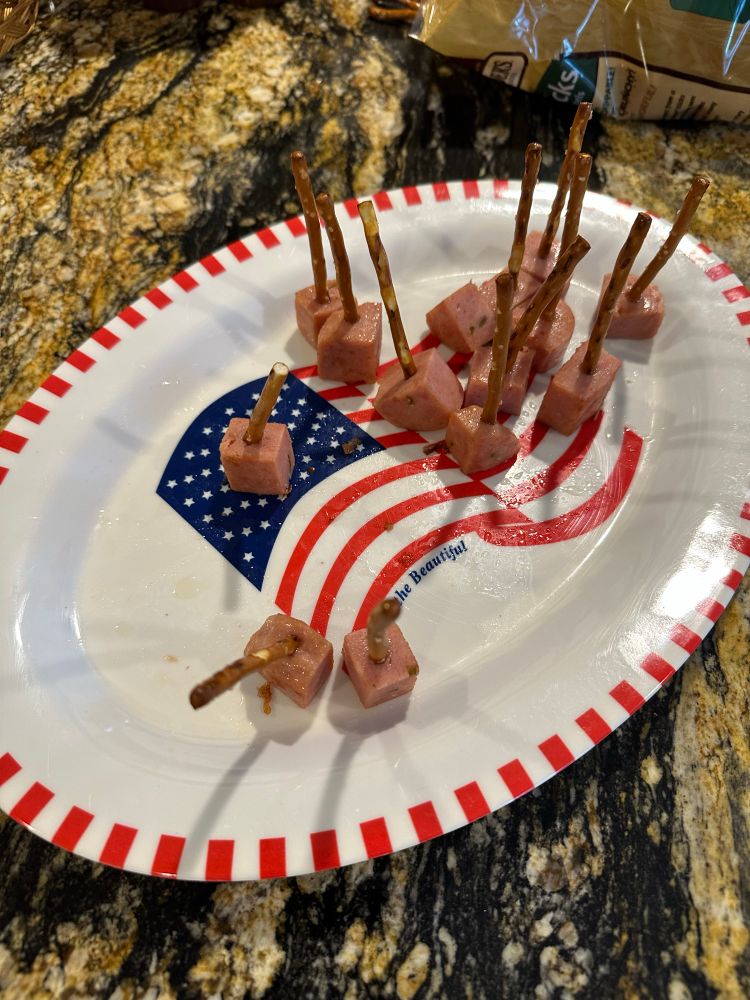 A mostly eaten tray of pan-fried Spam cubes impaled on pretzel sticks. 