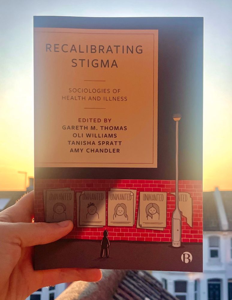 A copy of the book 'Recalibrating Stigma: sociologies of health and illness' edited by Gareth M. Thomas, Oli Williams, Tanisha Spratt, and Amy Chandler. The front cover of the book depicts a person out at night, lit by the light from a lamppost and looking at posters pasted onto a brick wall that are in the style of the 'WANTED' posters famously associated with the Wild West era of American history. The word 'UNWANTED' has replaced the word 'WANTED'.