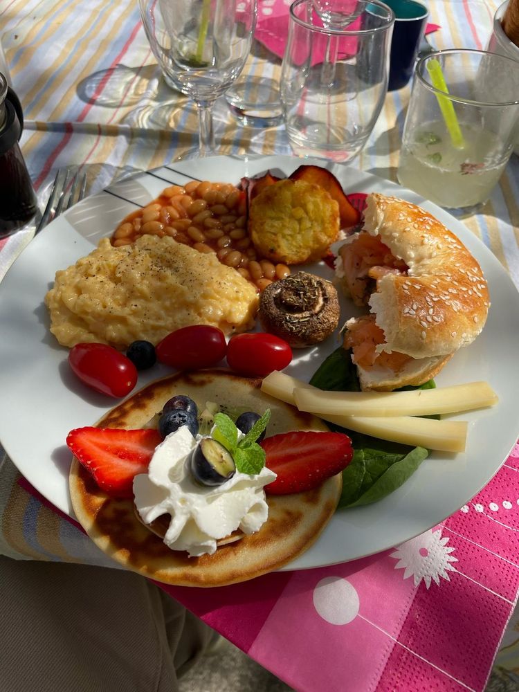 Assiette brunch composée d'oeufs brouillés, bacon, baked beans, rosti, champignon au four, tomates cerises, demi bagel truite fumée fromage frais, comté affiné 18 mois, pancake géant myrtilles fraises chantilly.