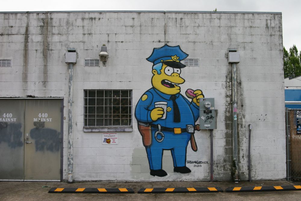 Mural of Officer Wiggum from The Simpsons on a drab industrial wall in an alley.