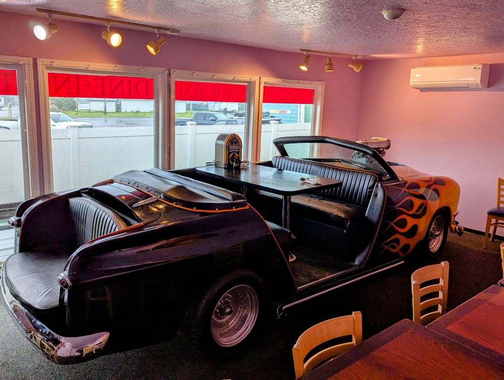 An old hot rod, black with flames on the front, converted to be a booth in a restaurant with a small jukebox on the table.  