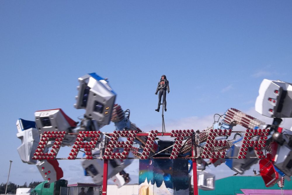 A carnival ride called "Orbiter" spins behind its sign made of many red light bulbs.  A legally distinct helmeted spaceman looms above.