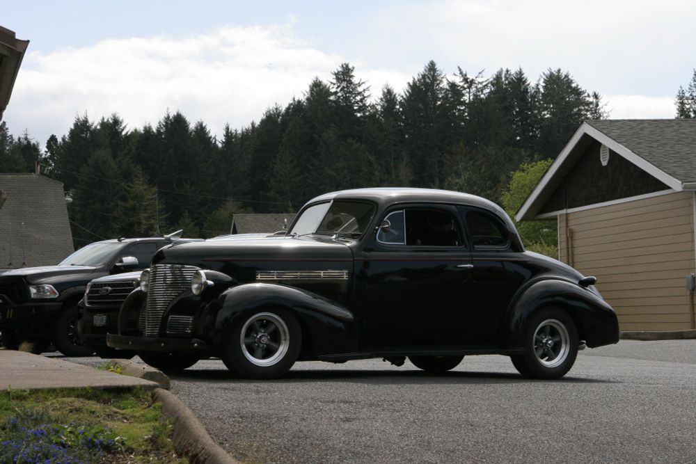 A lower angle, from the side and showing the front end of the car, also revealing its non-sandwich related surroundings: trees and another drab brown and tan building, this time vertical siding!  It's a bank.   