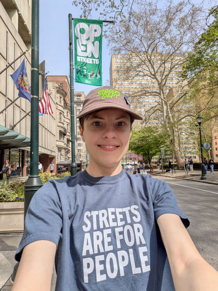 The poster wearing a Streets Dept hat and a "Streets are for people" shirt, in front of an Open Streets banner