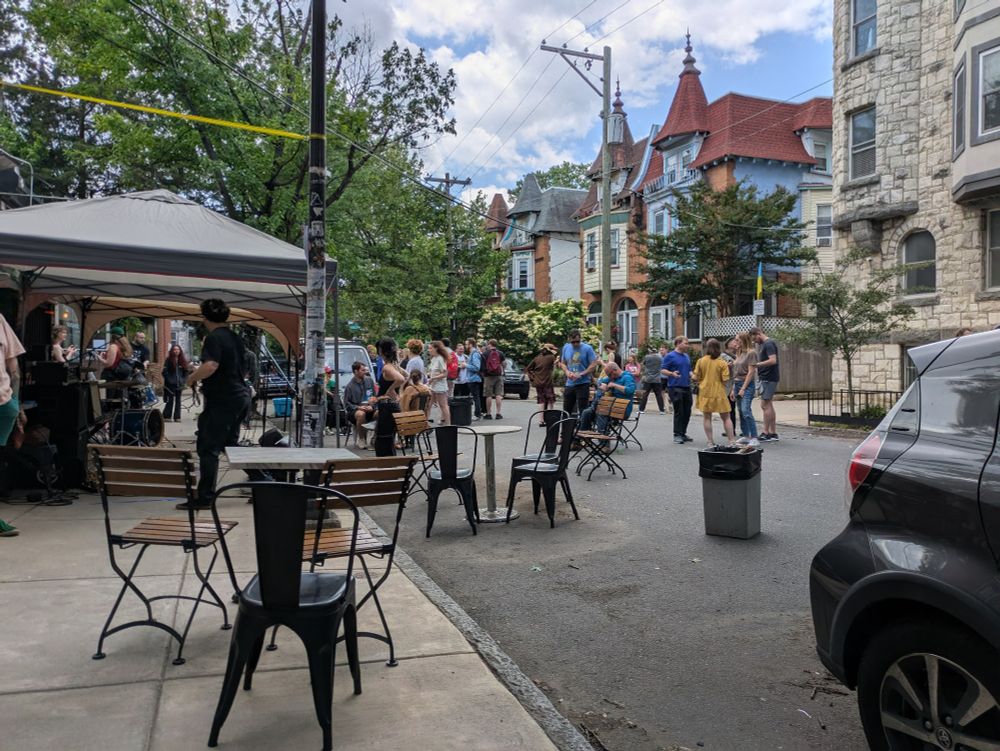 Another angle of a street that is filled with bistro tables and people standing around and chatting