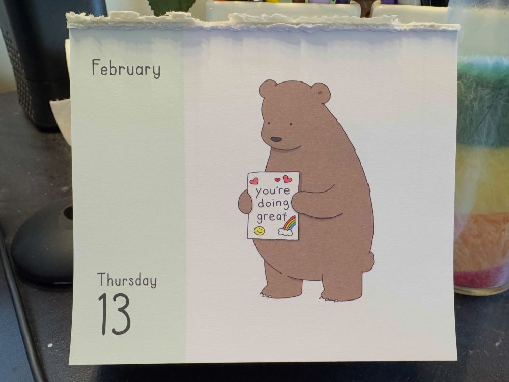 A calendar page from February Thursday 13 with a cartoon bear holding a sign that says "you're doing great" with colorful heart, smiley face, and rainbow doodles around it.