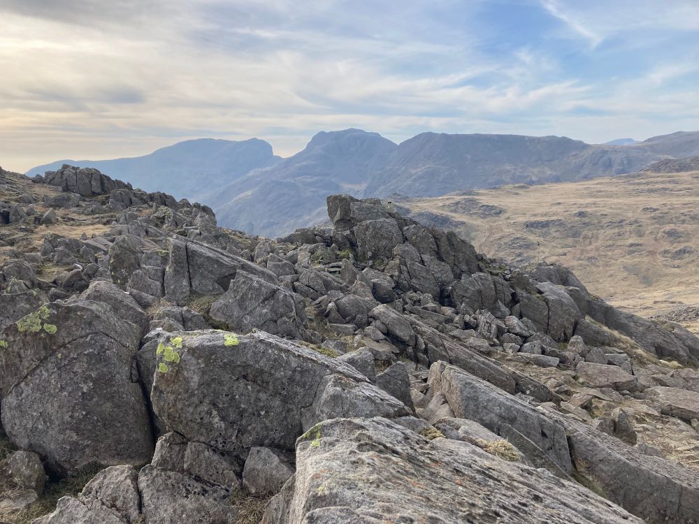 View across slanted rock outcrops in the foreground to Scafell Pike, England’s highest mountain, in the distance.