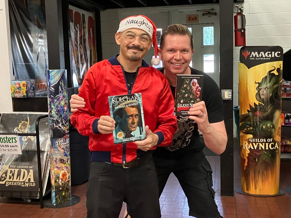 Authors Armando Munoz and Paul Terry at their book signing event holding each other’s books.