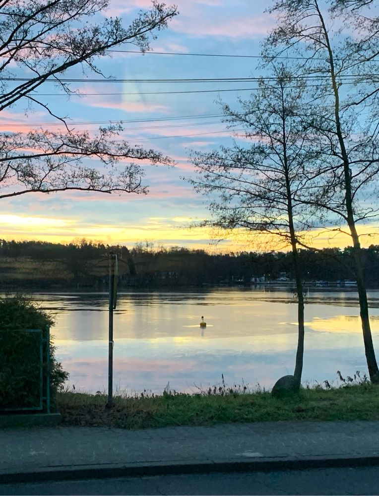 A lake with a blue, yellow and red sky above. 