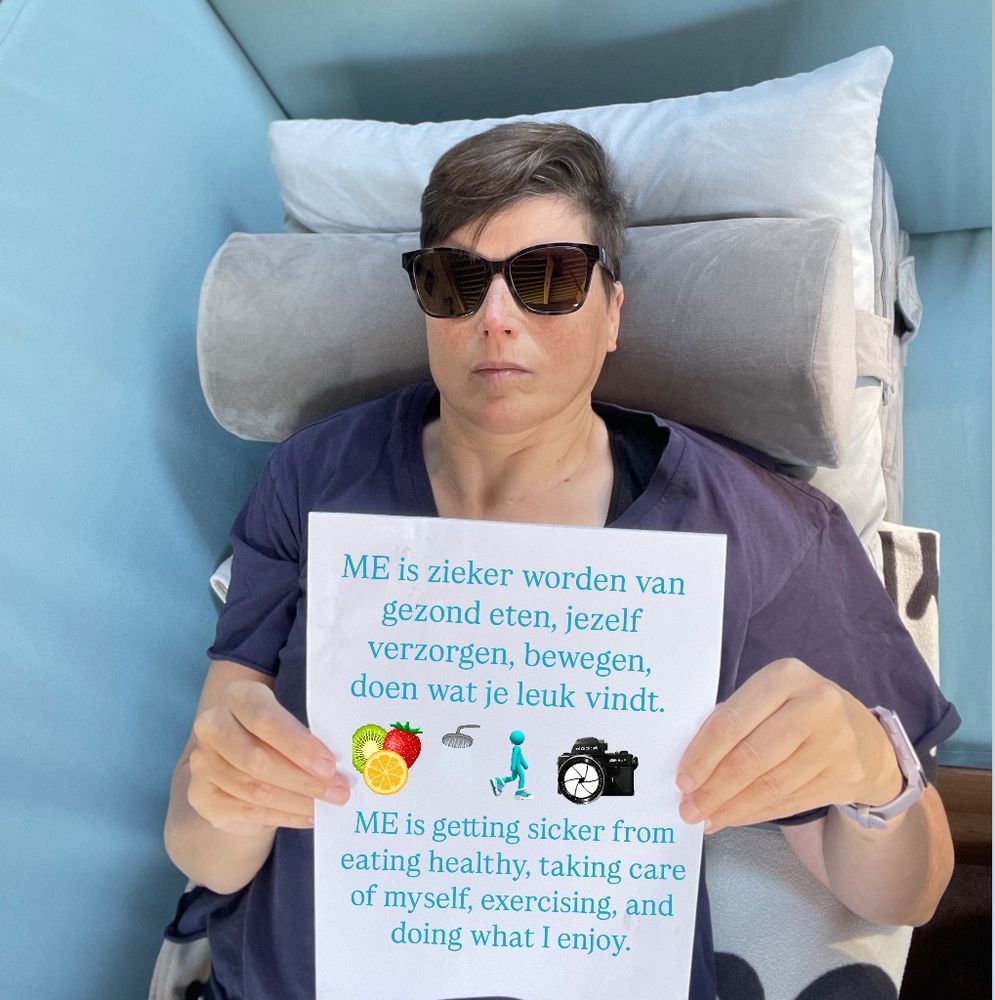 Vrouw met zonnebril op en blauw shirt aan ligt met een papier voor haar borst op een blauwe bank waarop in het Nederlands en Engels te lezen is:
ME is zieker worden van gezond eten, jezelf verzorgen, bewegen, doen wat je leuk vindt.
