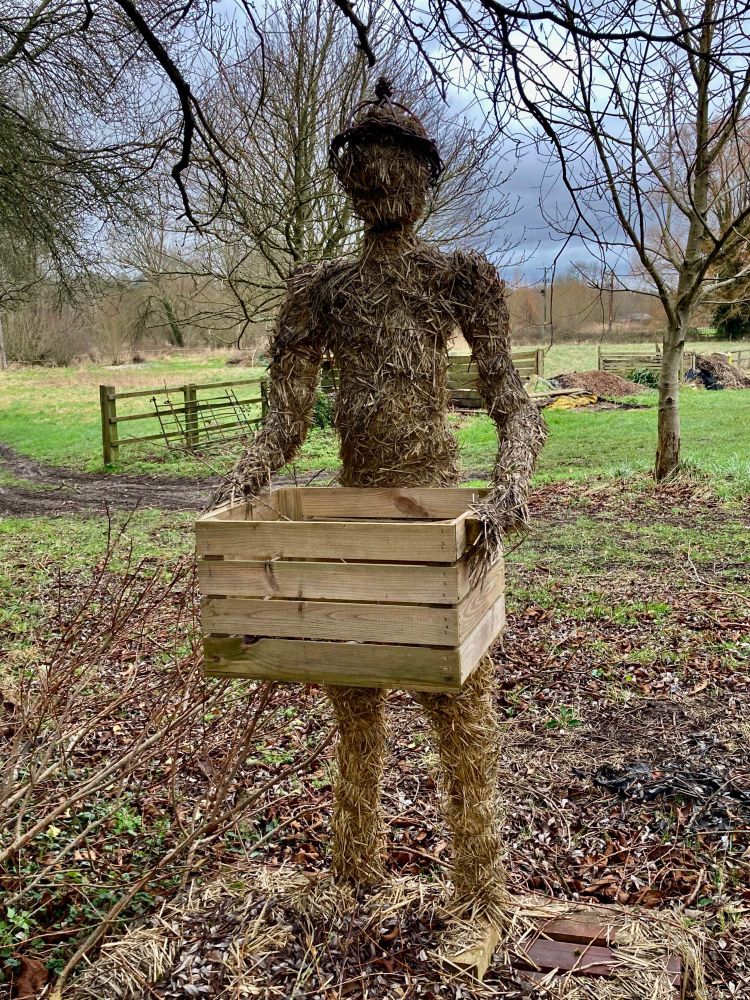 Straw figure of a person holding a wooden box.