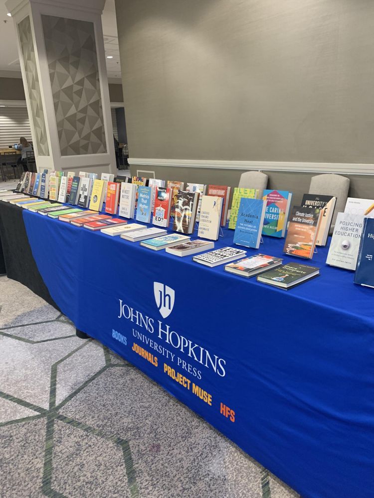 The Hopkins Press exhibition table at ASHE 2025, focusing on a long display of new books