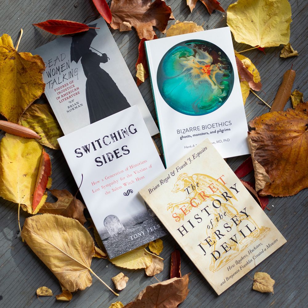Books from Hopkins Press on a gray wooden background surrounded by autumn leaves.
