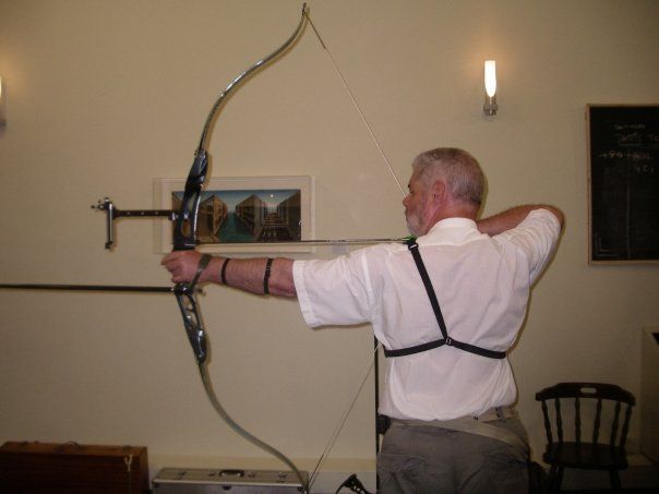 Archer facing away from the camera with a recurve bow at full draw, indoors, shooting in an archery darts competition