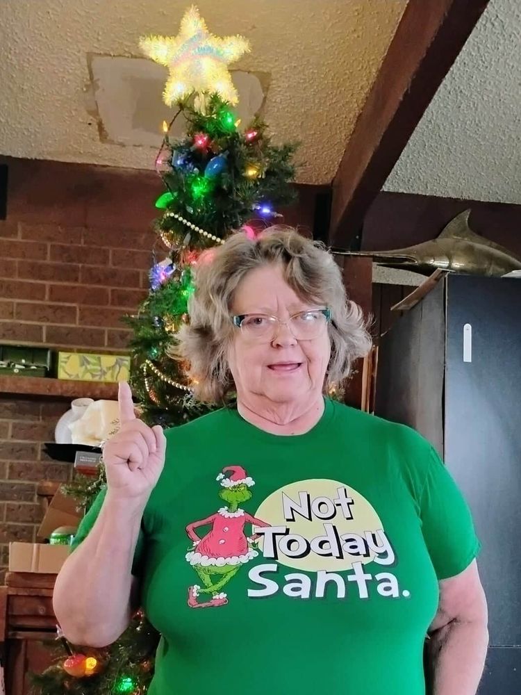 A woman is standing in front of a Christmas tree. Her t-shirt shows the Grinch in a Santa costume. The caption says, "Not today, Santa."