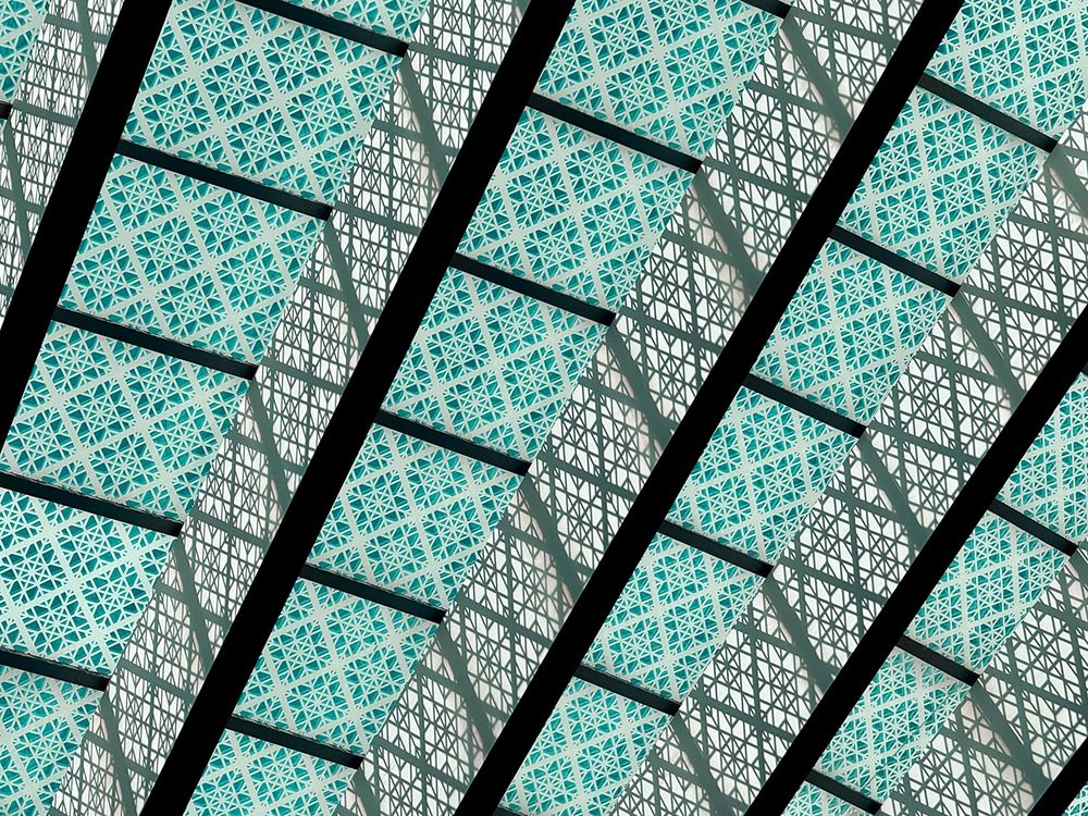 An abstract image of patterned glass casting shadows upon the support beams holding the glass ceiling up.