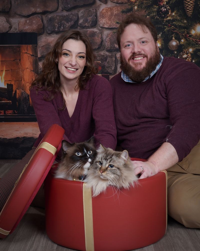 A couple in matching red sweaters with their two cats in a present box