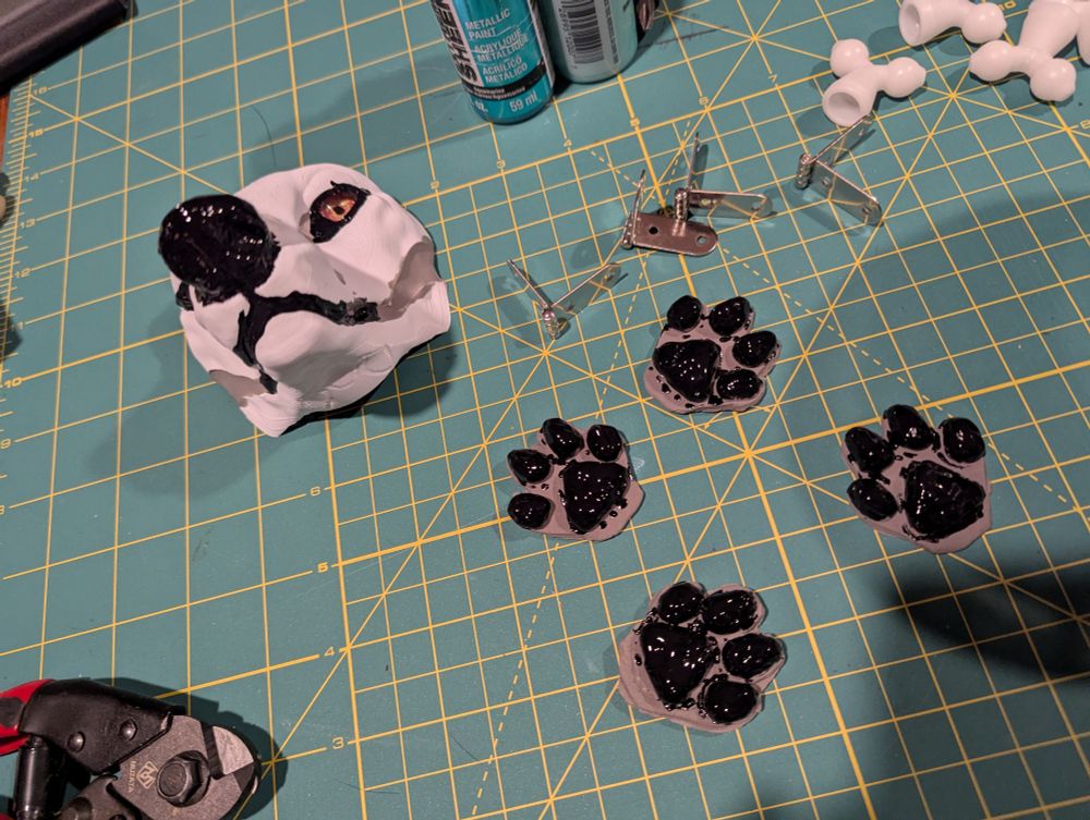 A small layout of a small canine fursuit head with gold eyes and four paw pads. Nose, mouth, around the eyes, and all of the paw pads are now painted with slick paint