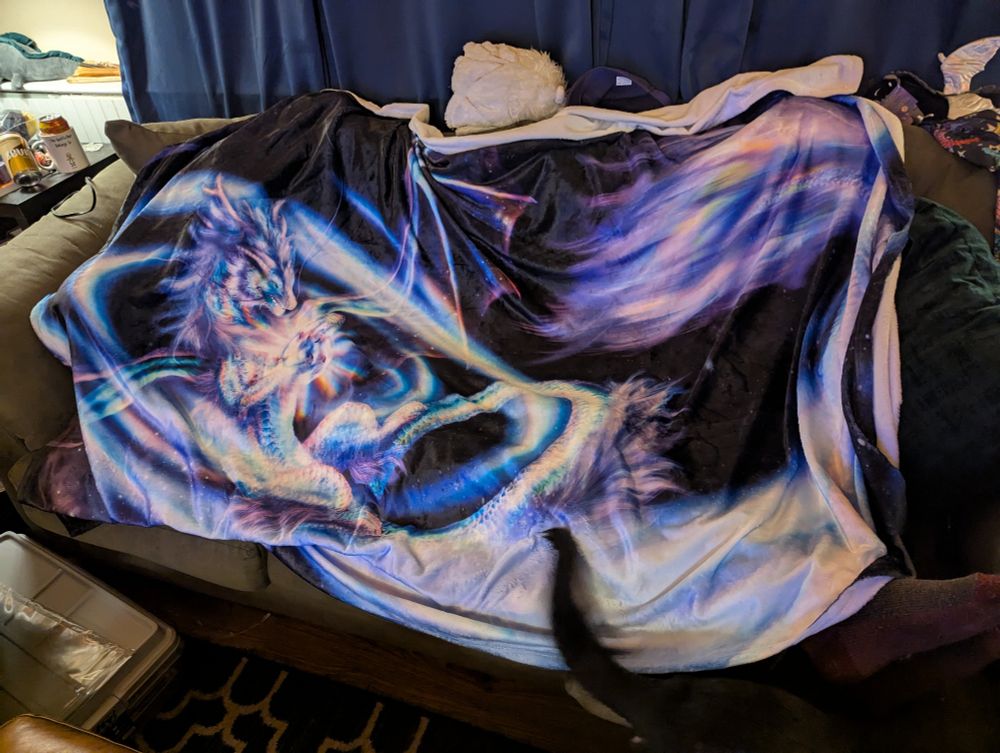 A large very soft blanket decorated with art of a holographic dragon holding an orb and casting swirling magic. 