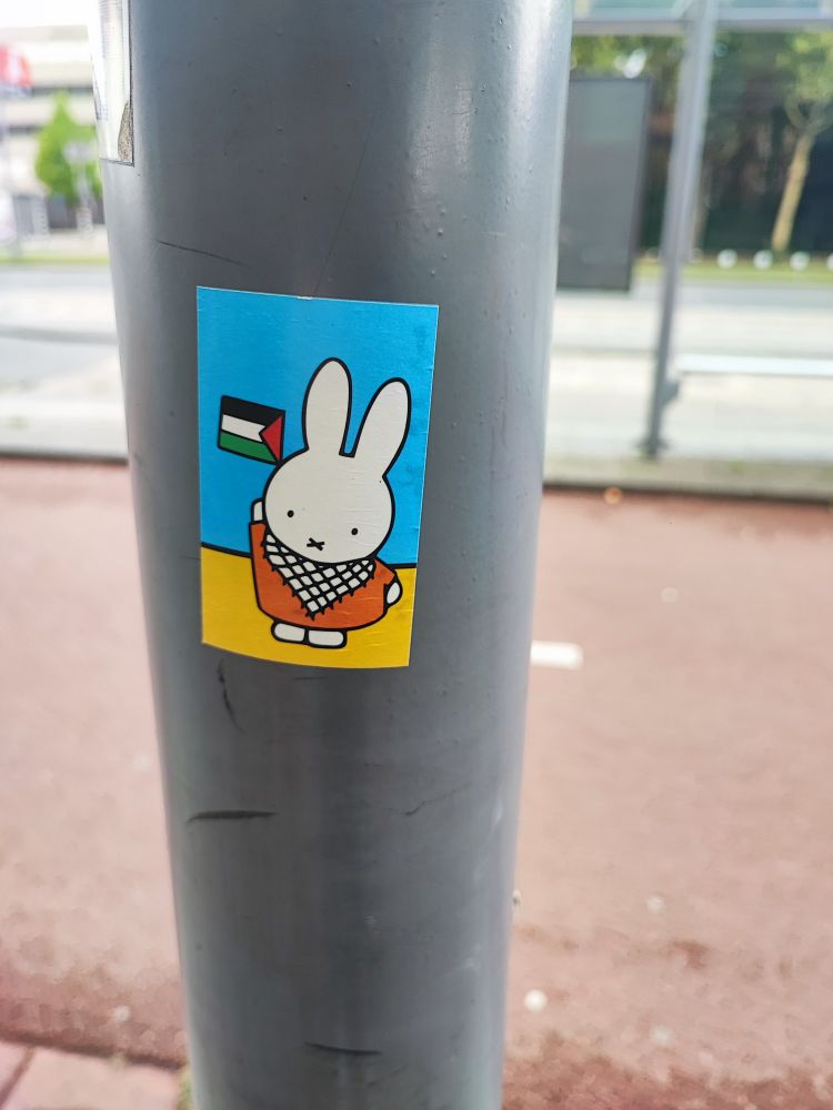 A sticker of Miffy, als known in Dutch as Nijntje, wearing a keffiyeh while raising a Palestinian flag.