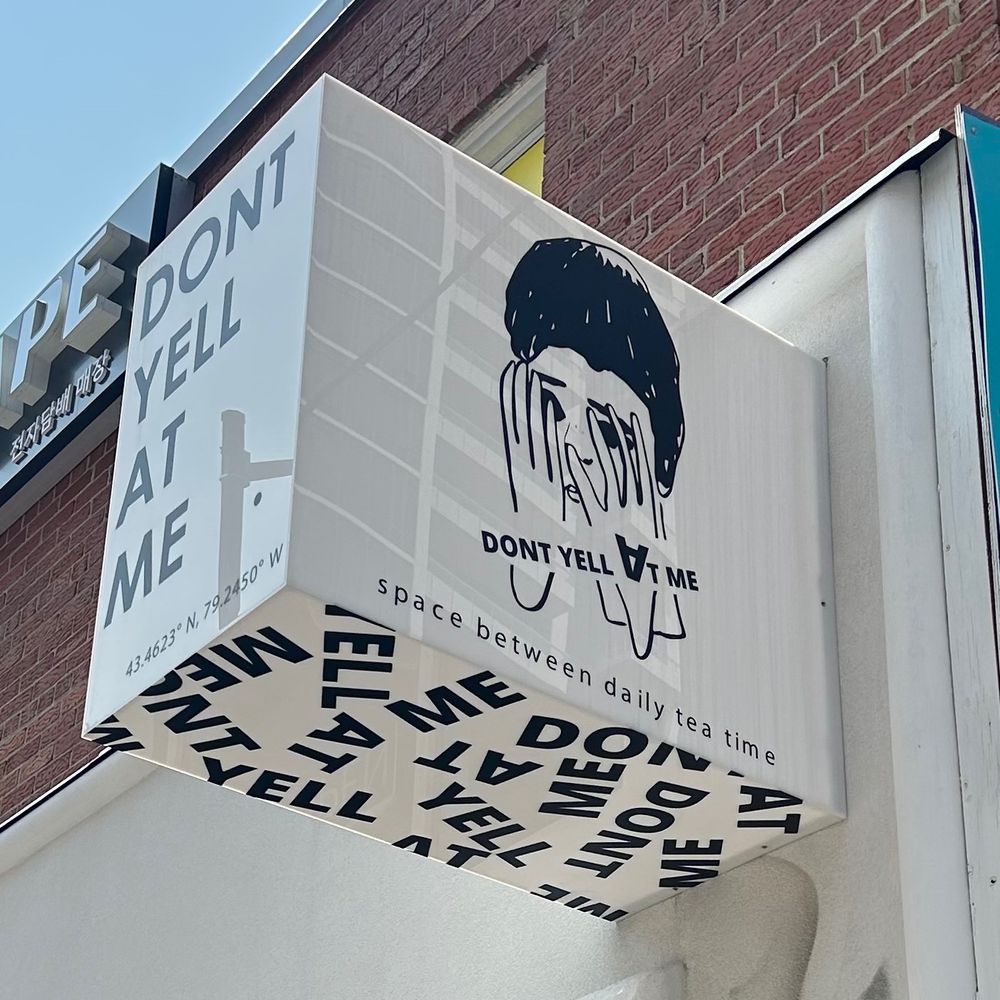 Sign of a tea shop called “Don’t yell at me”, featuring an illustration of someone hiding their face with their hands