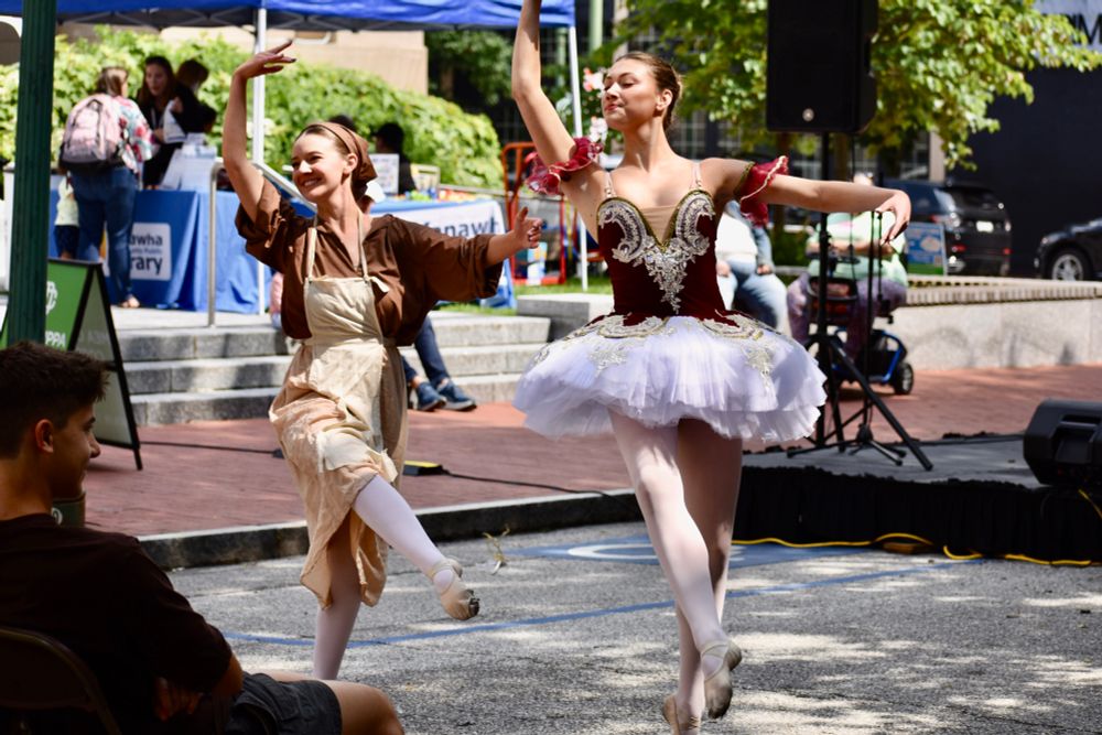 A ballerina dressed as Cinderella in rags and another in a fairy godmother costume dance en pointe in a street performance. 