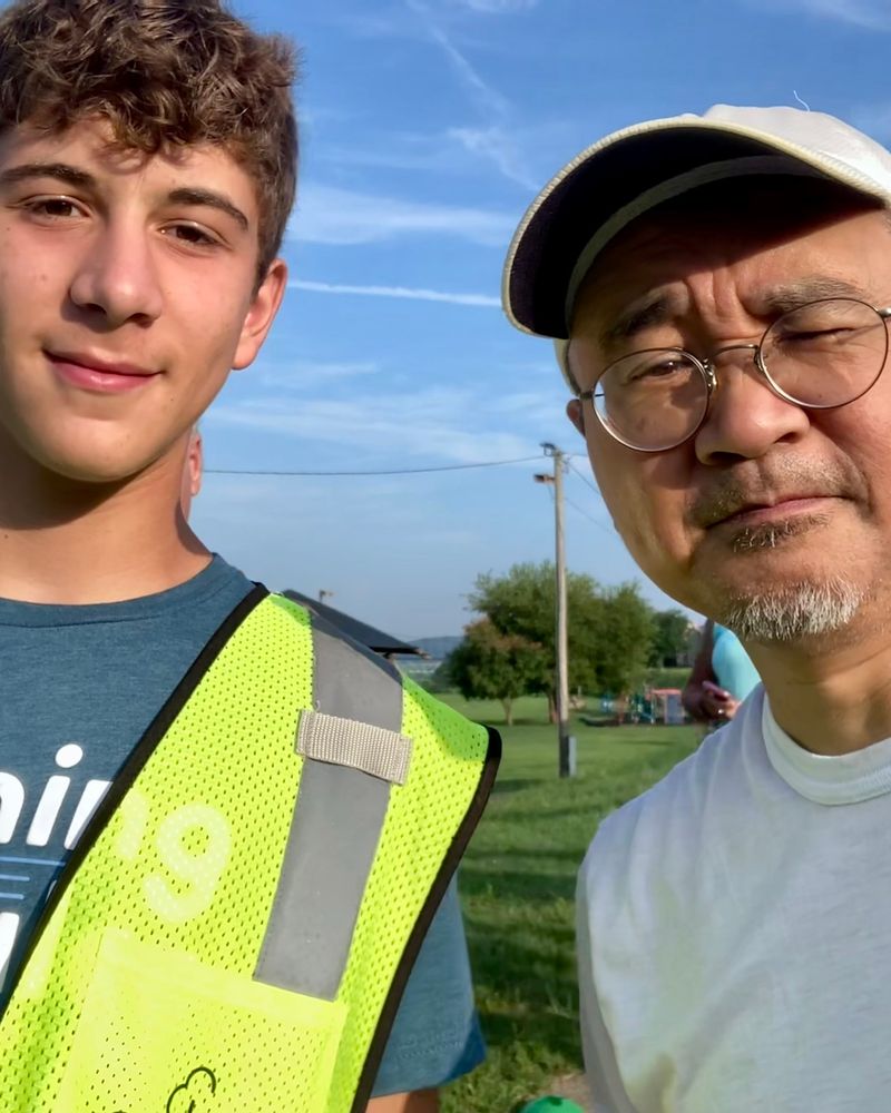 Selfie of student volunteer wearing a Parkrun hazard vest next to middle-aged man squinting in the morning sun. 