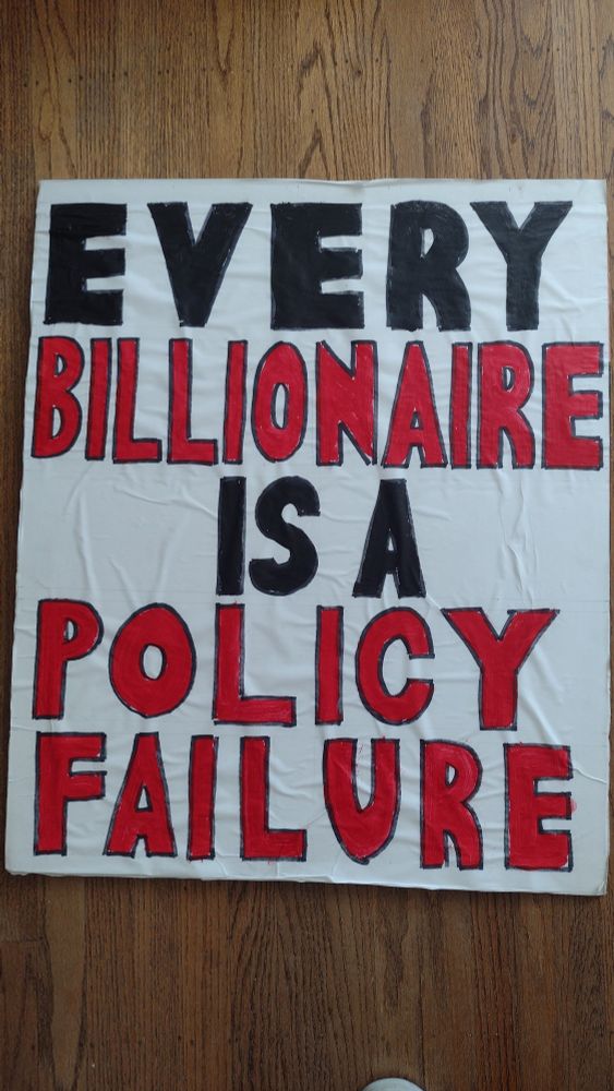 Protest sign: EVERY BILLIONAIRE IS A POLICY FAILURE 