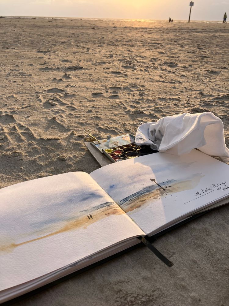 Open sketchbook lying on the beach sand showing a sketch of said beach, St Peter-Ording, North Sea