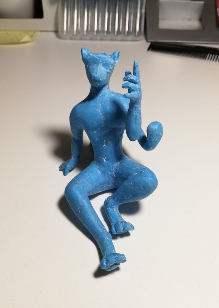 A handmade figurine of Zyyph - a snow leopard fursona.
The figure is sitting down and leaning back with one hand help up and other bracing against the ground. It is facing towards the viewer. An unfinished figurine, made from blue PLA using a handheld 3D-printing-pen. The surface is smooth after cleaning up with a solder and sandpaper.