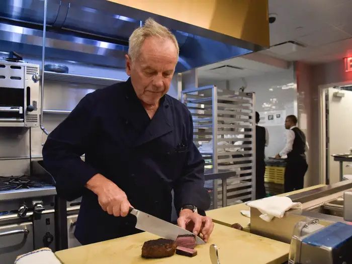 A picture of Wolfgang Puck, that celebrity chef, cutting a peace of what looks like lamb or beef