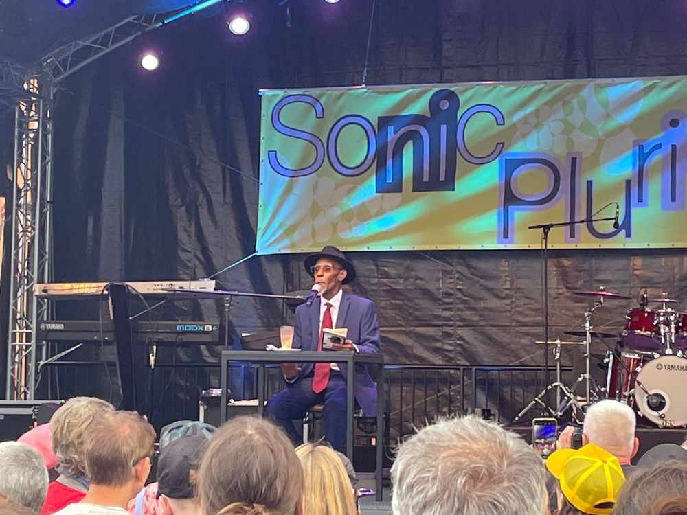 Linton Kwesi Johnson with hat and suit sitting on the stage of HKW