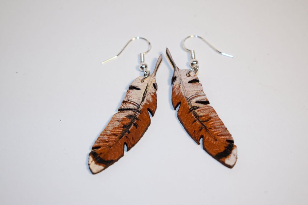 Custom leather earrings in the shape of feathers painted to loom like red tailed hawk feathers. These can be made to look like many different bird species or can be painted with pride flags or other similar designs and ideas.