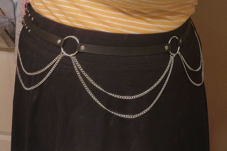 A photo of a punk style leather and chain belt handmade by birdy and available on her shop. The belt is made of black leather, silver rings and draping chains between them.