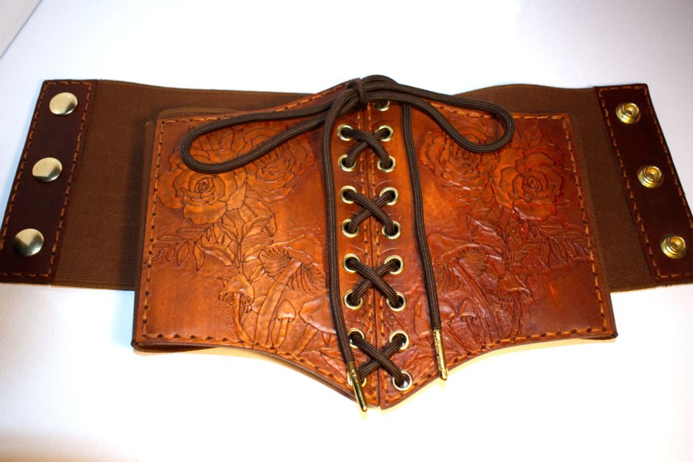 A custom and hand crafter leather corset belt with detailed tooling of roses and mushrooms. These belts can be made to order and deeply customized for whatever look you are going for