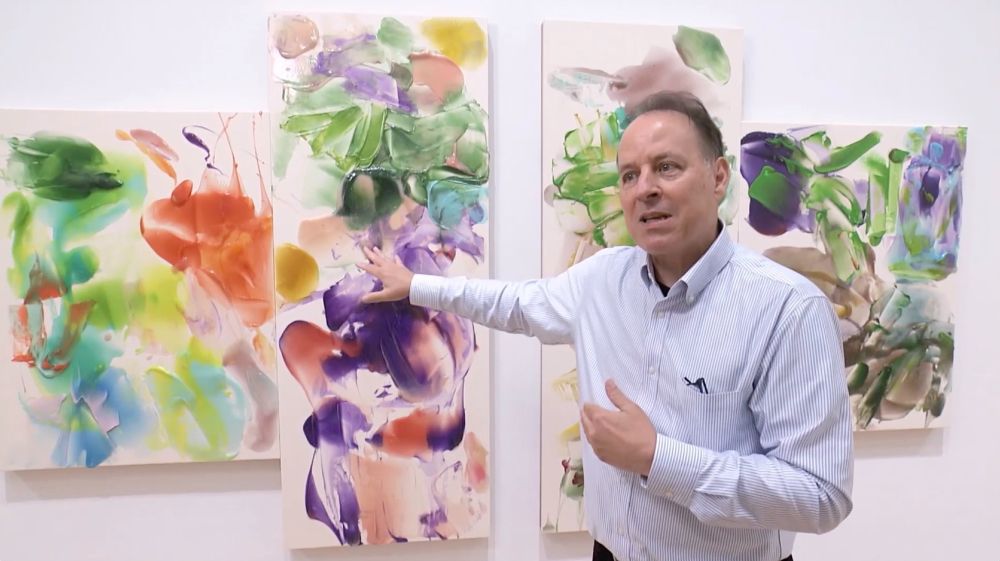 Artist and writer Azby Brown speaks in front of a painting by Kenjiro Okazaki. The image is a screenshot from NHK's Nichiyo Bijutsukan TV show.