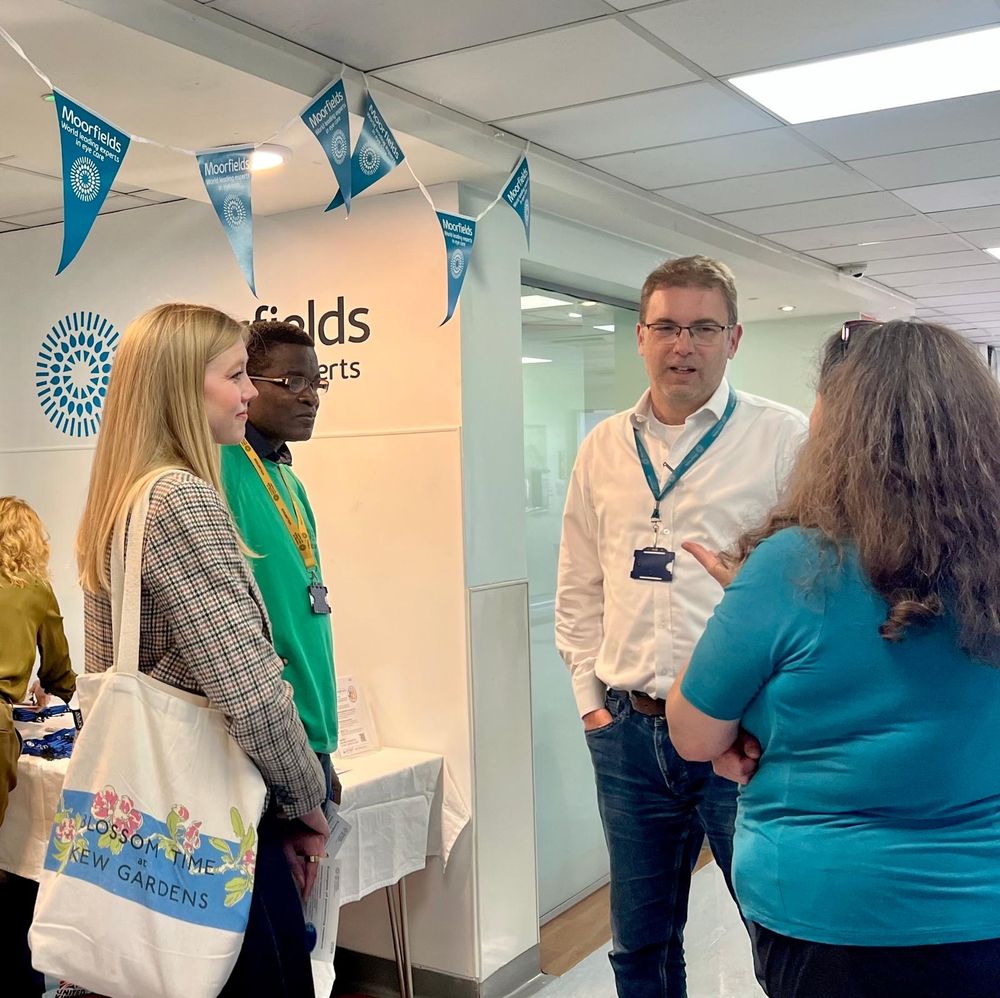 Pearse Keane stands chatting with three visitors at the entrance to the exhibition space in Moorfields Eye Hospital main corridor