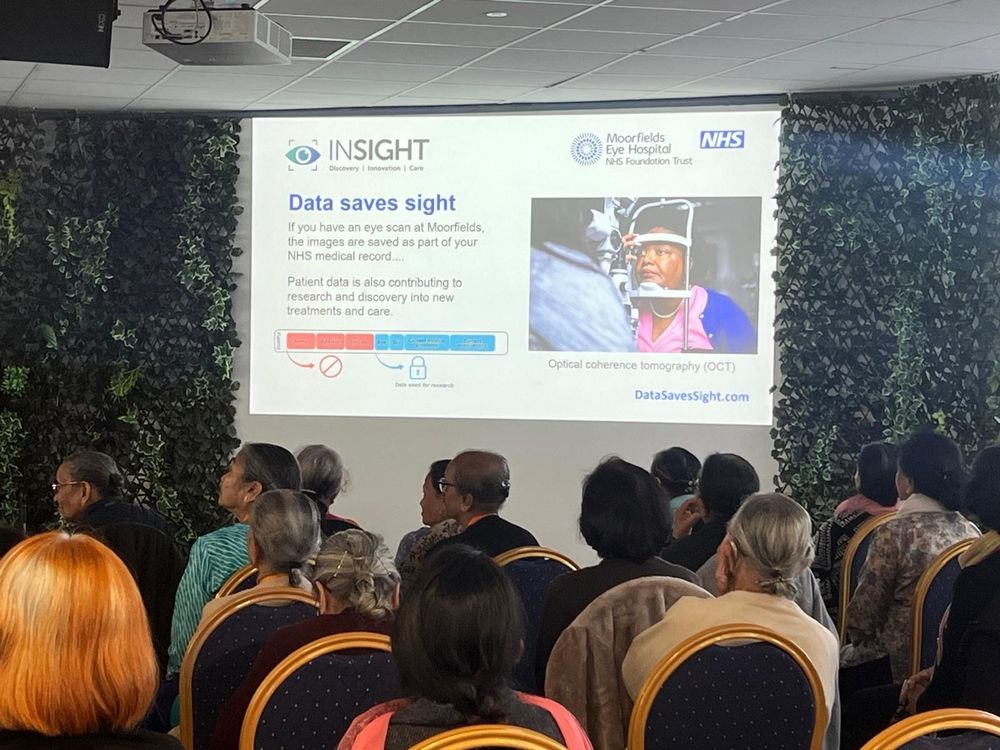 Data Saves Sight presentation slide on a large projector screen, with people seated in the foreground