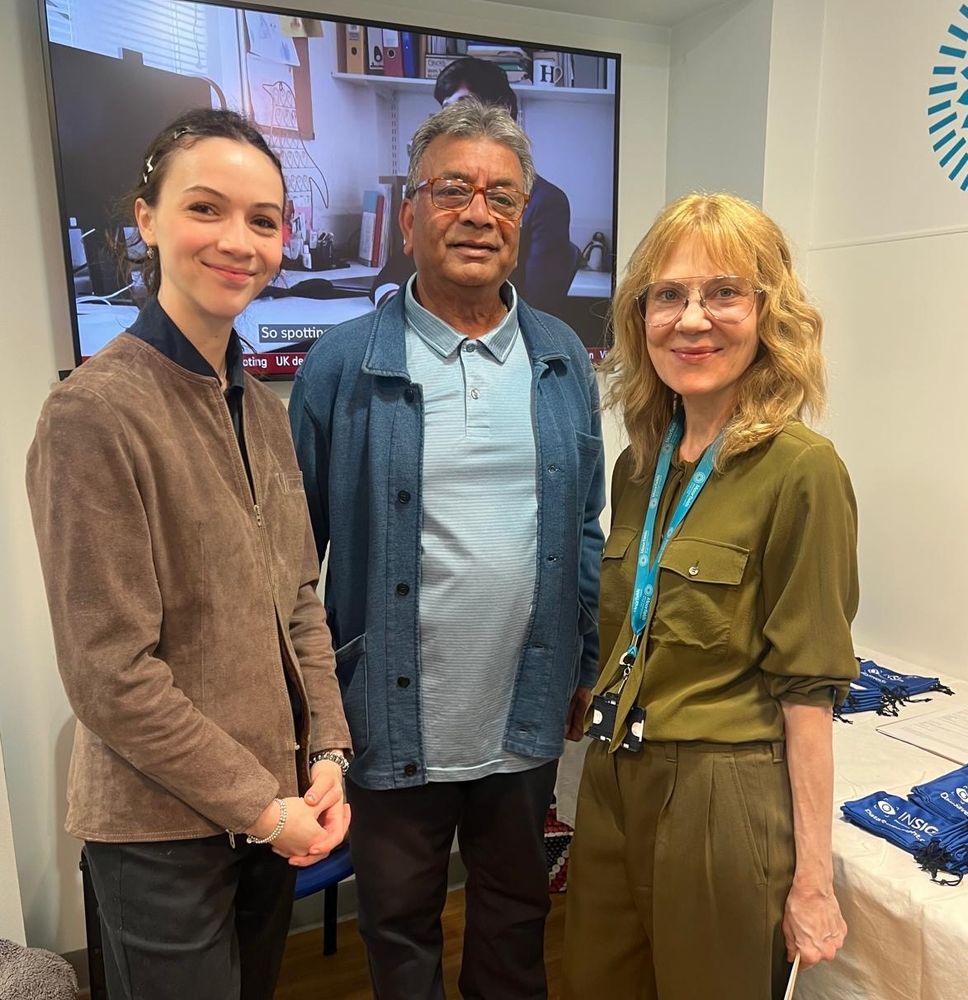 Three people - visitors and the INSIGHT team - smile to the camera during the pop-up event, against the white walls of the exhibition space at Moorfields Eye Hospital