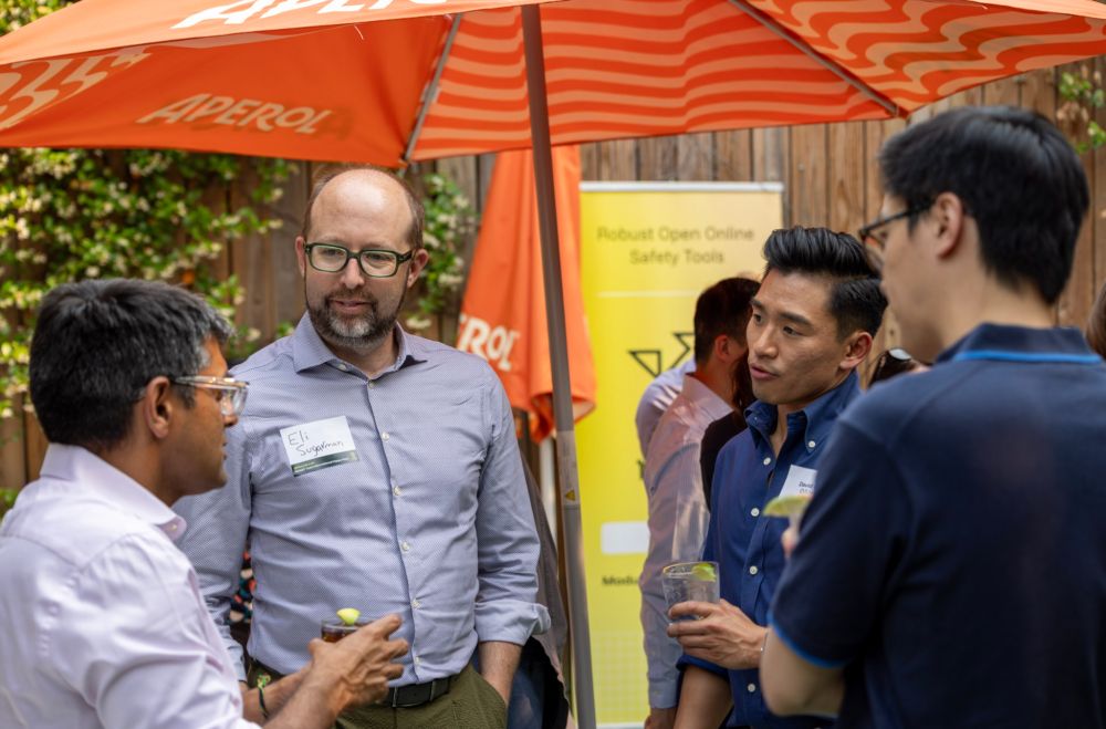 Four attendees chat at the event, with ROOST signage featuring in the background. 