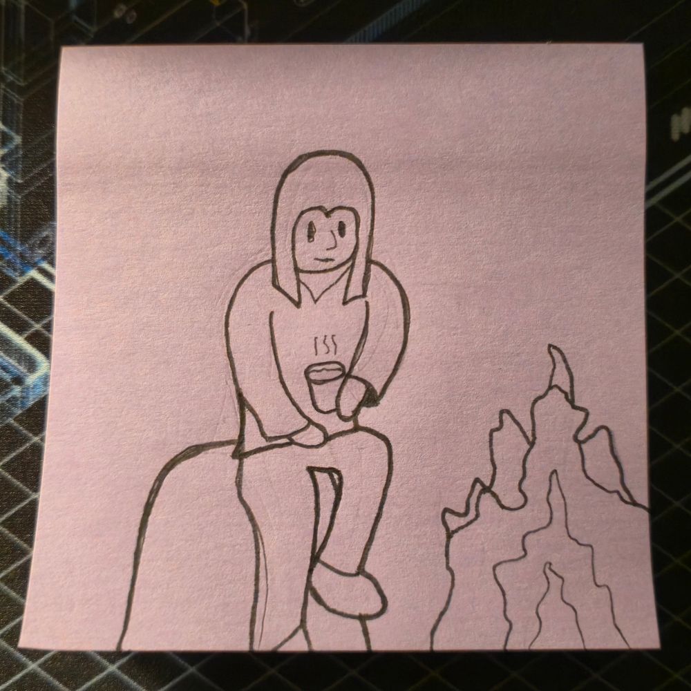 A man sits on a rock, holding onto a steaming hit drink. A campfire burns in front of him.