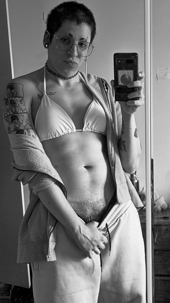 A selfie of Sable in the mirror. She's holding her phone in one hand, and pulling her pants down with the other, showing her bush and teasing you, with a pouting face 