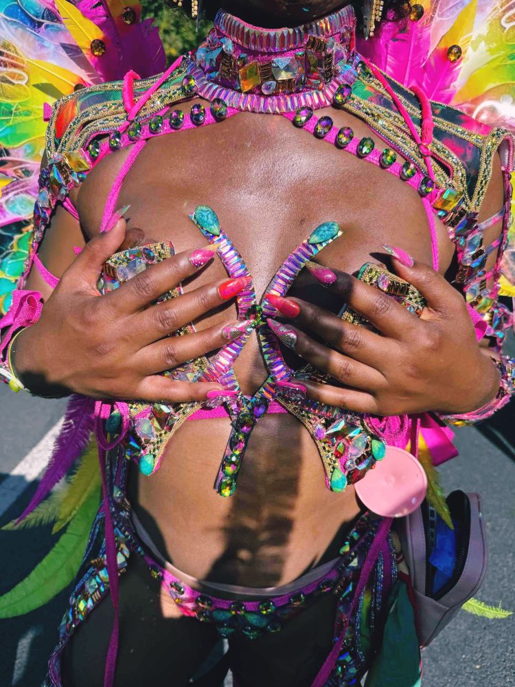 Photo of me from the neck down in a carnival costume. My is covered in gems in shades of green, pink, and yellow. My hands are over the wire bra piece showing off my custom made press on nails. 