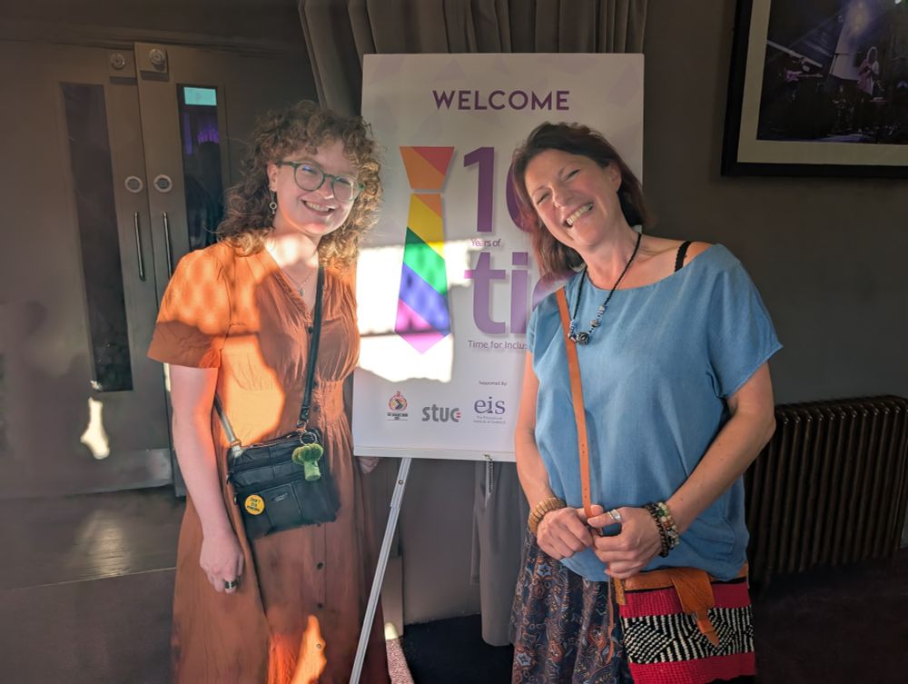 Two members of WOSDEC stand in front of a sign saying welcome, 10 years of TIE.