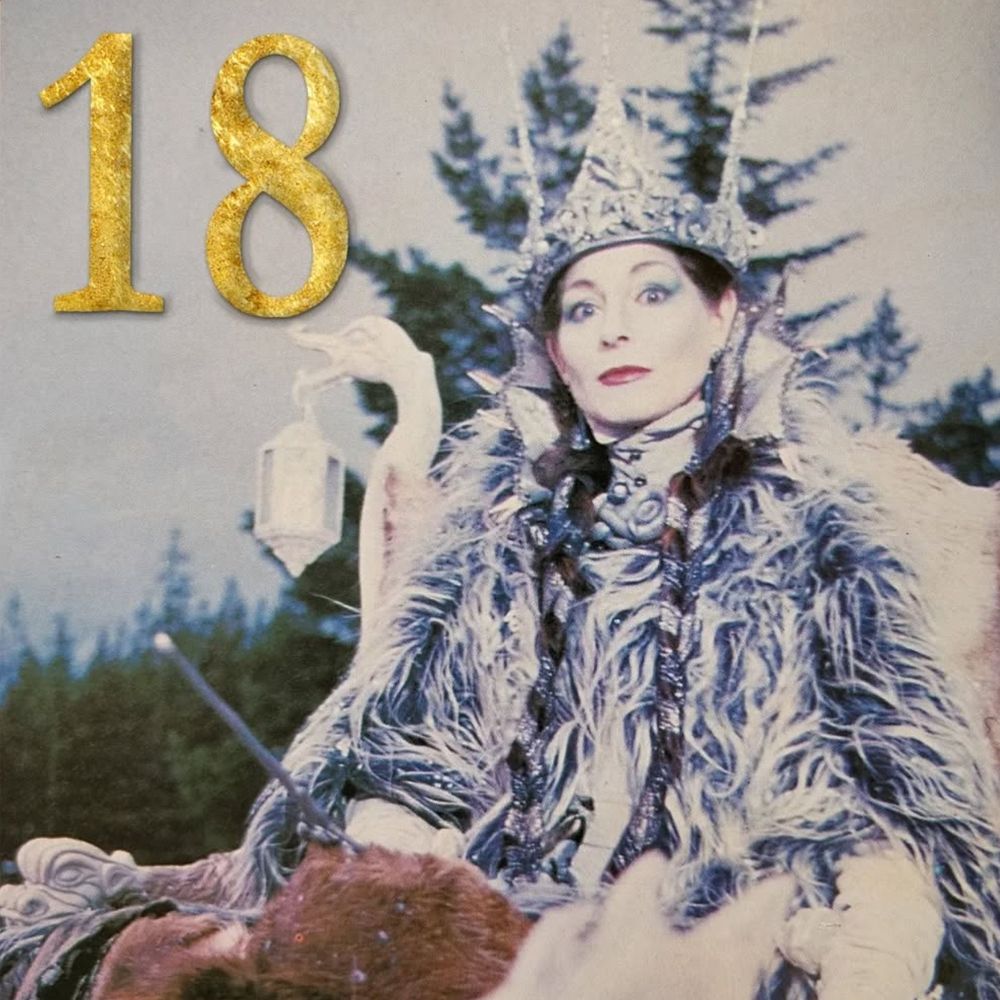 The White Witch, with a piercing stare, sits, a menacing figure, dressed in furs, with a sharp white crown on her head.