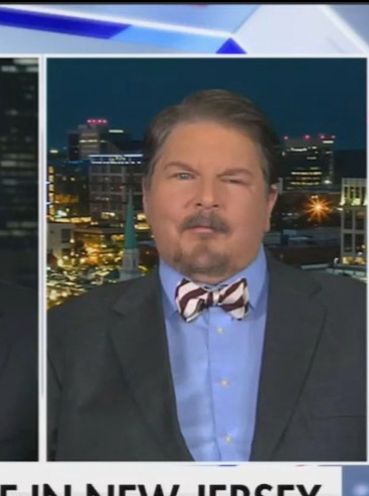 Closeup of Fox News guest wearing gray sport coat, blue shirt, and striped white bow tie. 