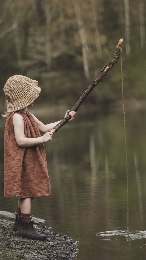 une petite fille au bord de l'eau qui pèche avec un morceau de bois 